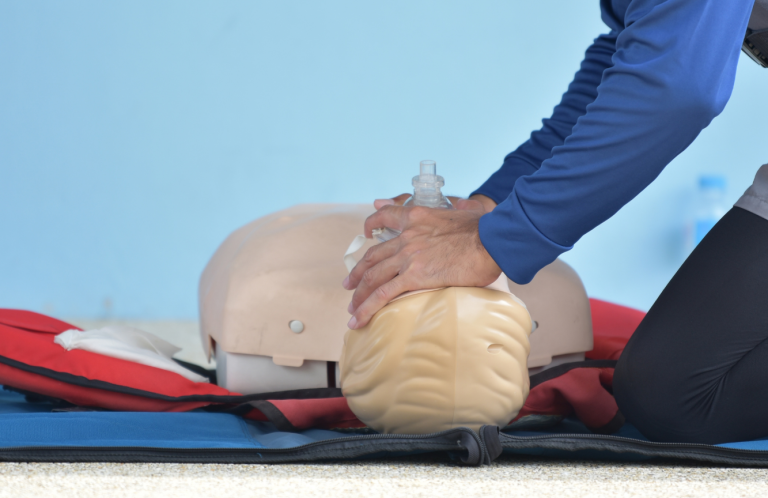 A person performing CPR on a training manikin on a mat.