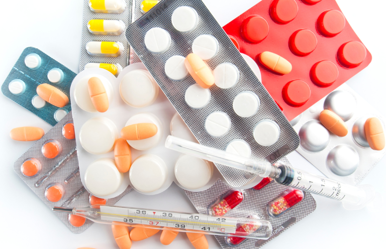 Assorted tablets, capsules, and a syringe scattered across a surface.