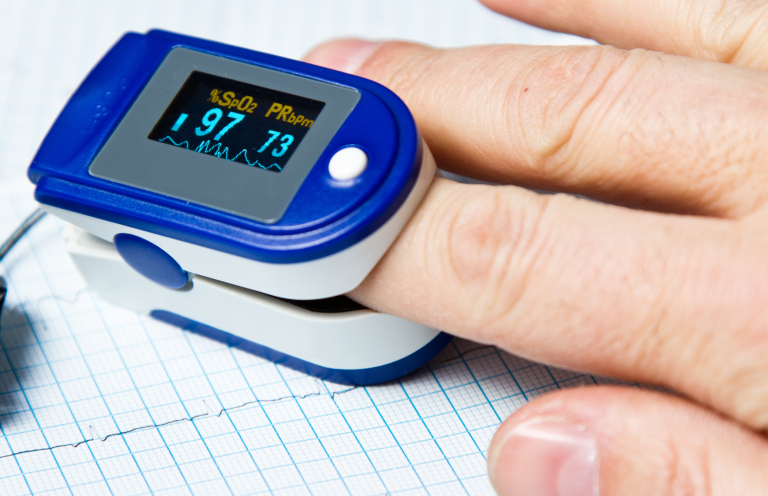 A finger being monitored by a pulse oximeter displaying heart rate and oxygen levels.