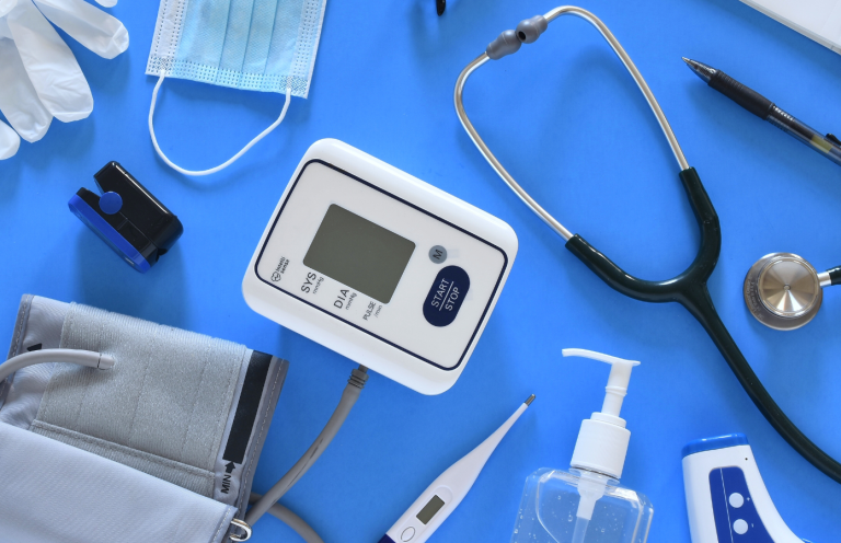 Blood Pressure Measurement Training Medical equipment including a blood pressure monitor, gloves, and sanitising gel on a blue surface.