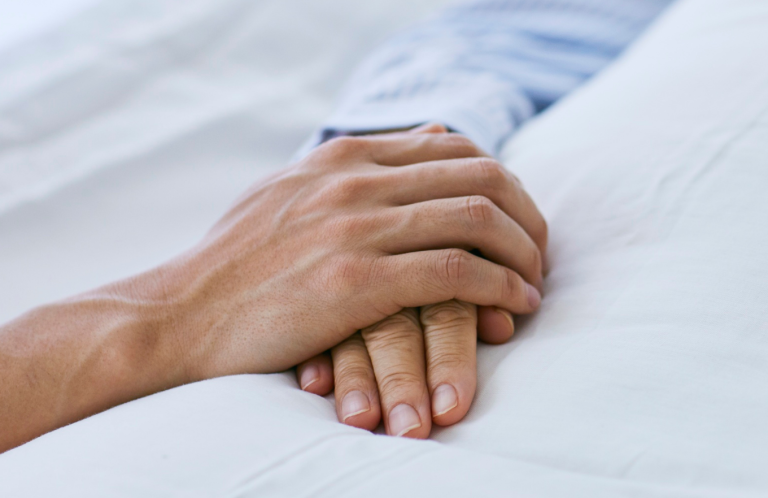 End of Life Care Two hands gently clasped together on a soft surface.