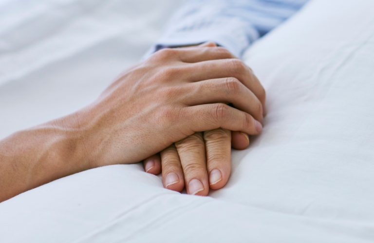 End of Life Care Two hands gently clasped together on a soft, white surface.