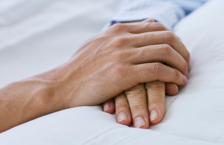 Two hands clasped together on a soft surface.