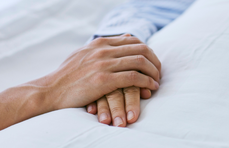 Two hands clasped together gently on a soft surface.