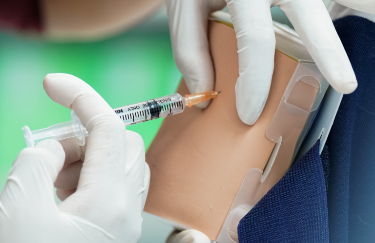 A hand administering an injection into a medical training prosthetic.