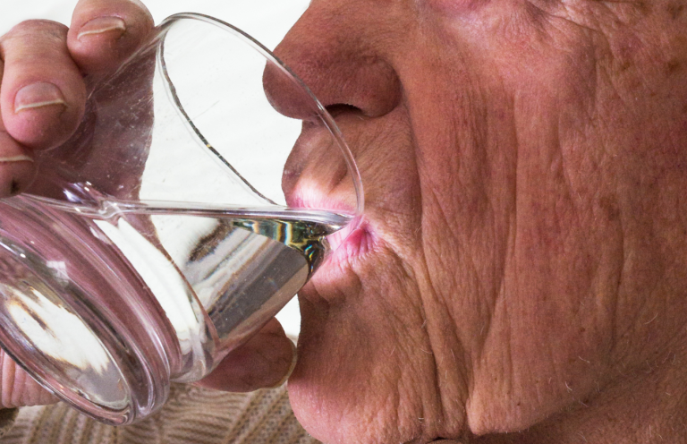 Elderly person drinking water from a glass, highlighting facial wrinkles.