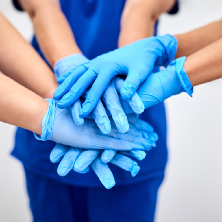 Safer Patient Care Several hands wearing blue gloves stacked together in a collaborative gesture.