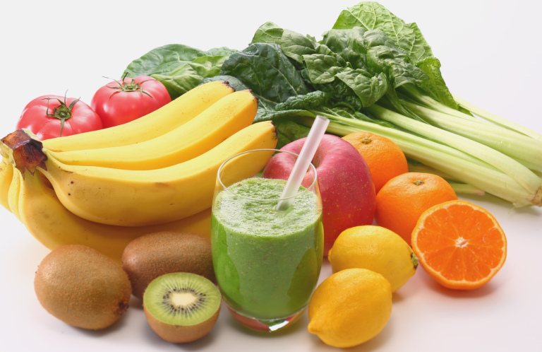 A variety of fruits and vegetables with a green smoothie in a glass.