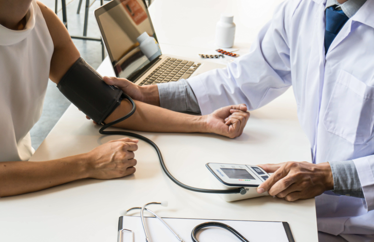 Recognising a Deteriorating Patient A doctor taking a patient's blood pressure at a desk with a laptop.
