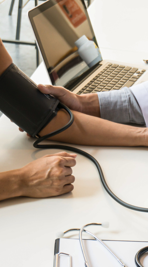 Recognising a Deteriorating Patient A healthcare professional taking a patient's blood pressure at a table with a laptop.