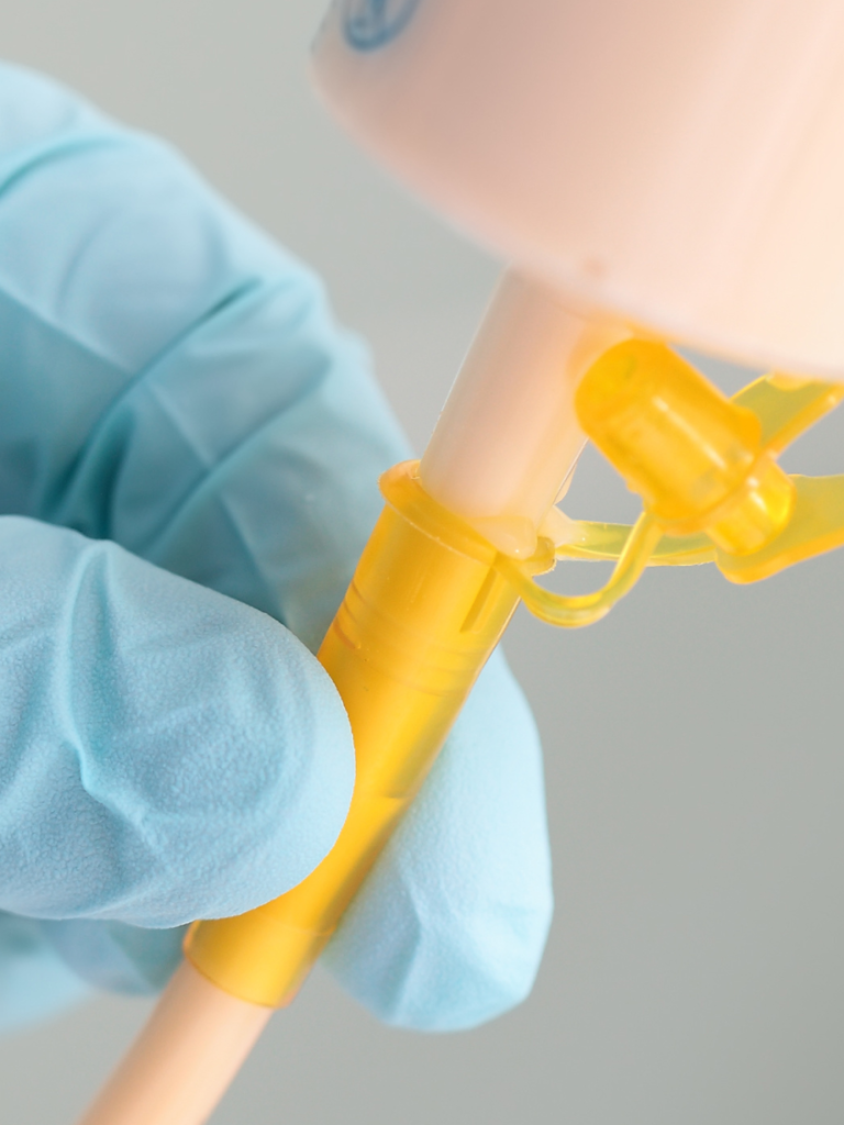 A gloved hand holding a medical device with a yellow attachment.