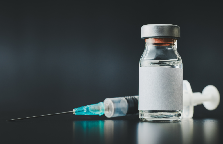 Vial of vaccine with a syringe and needle on a dark background.