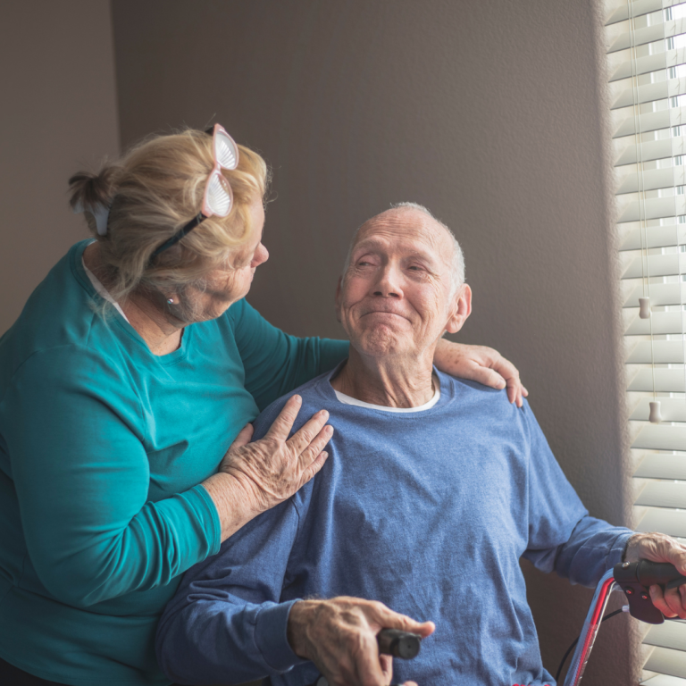 Complex Care Needs A woman affectionately speaks with an elderly man in a bright room by a window.