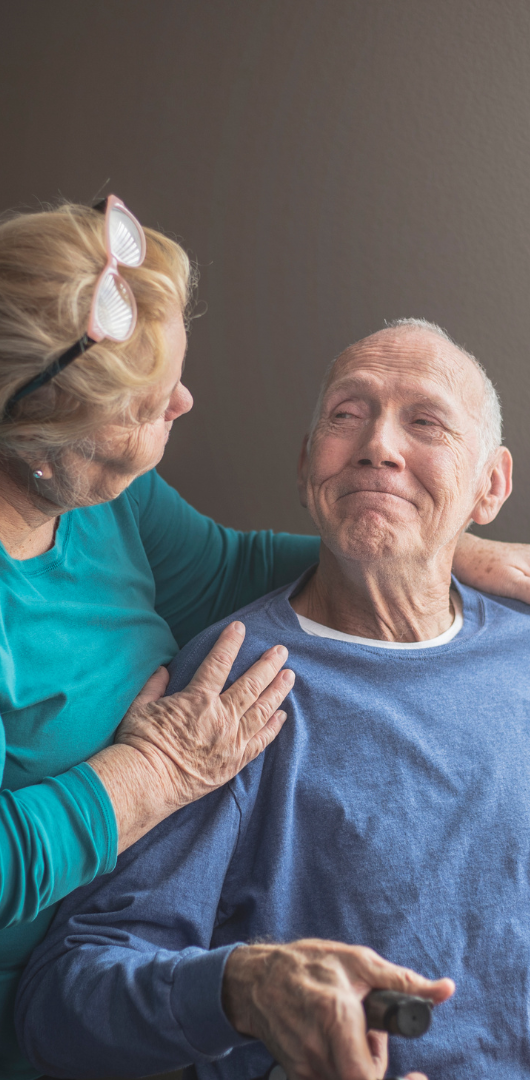 Dementia Awareness Training An elderly man smiles warmly as a woman softly touches his shoulder.