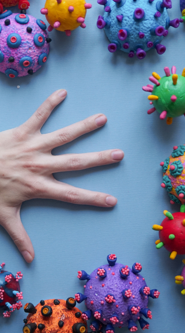 Infection Prevention and Control A hand surrounded by colourful virus models on a blue background.
