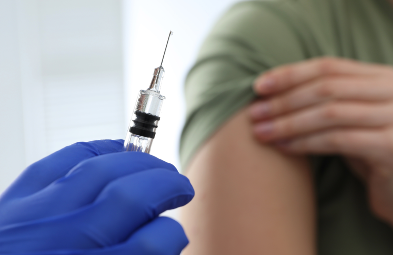 A gloved hand holds a syringe near a person's arm ready for vaccination.