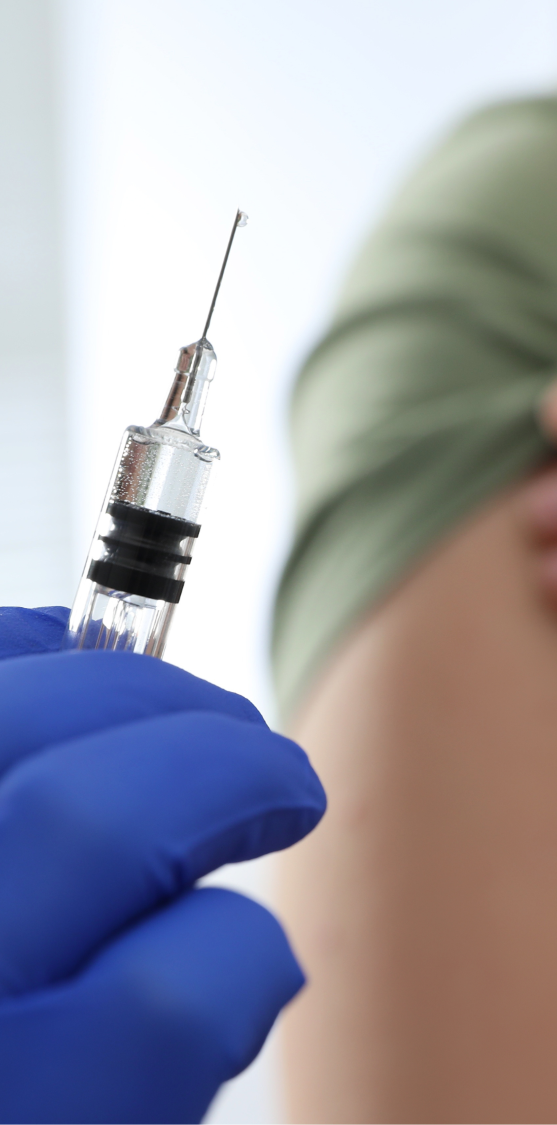 A gloved hand holding a syringe approaching an exposed shoulder.