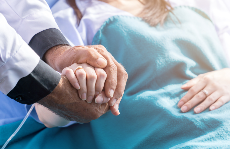 A doctor holds a patient's hand supportively in a healthcare setting.