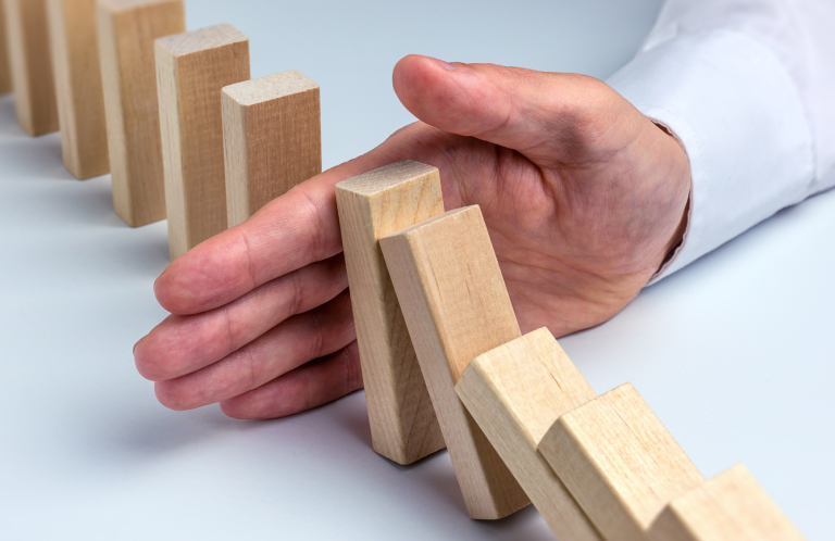 A hand stopping wooden dominoes from falling over in a row.