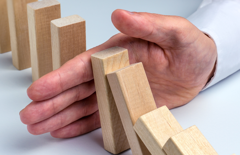 A hand stopping wooden dominoes from falling over.