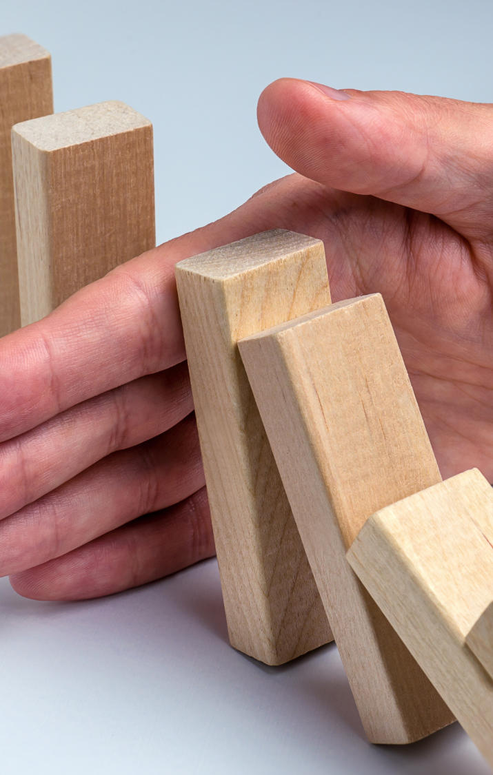 A hand supports a falling wooden block among upright blocks.