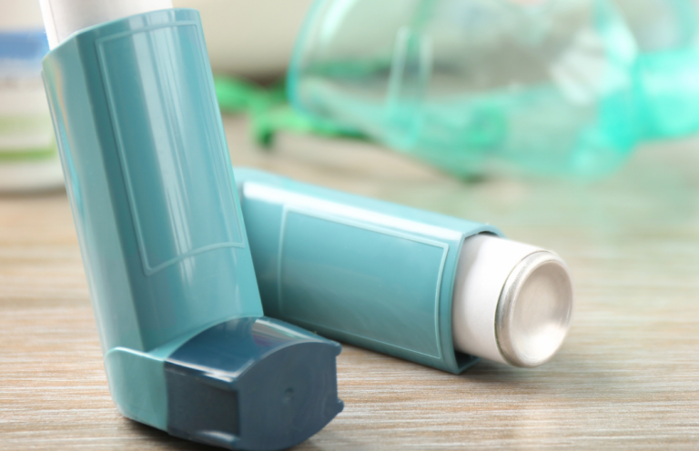 Two teal inhalers placed on a wooden surface, with a nebuliser in the background.