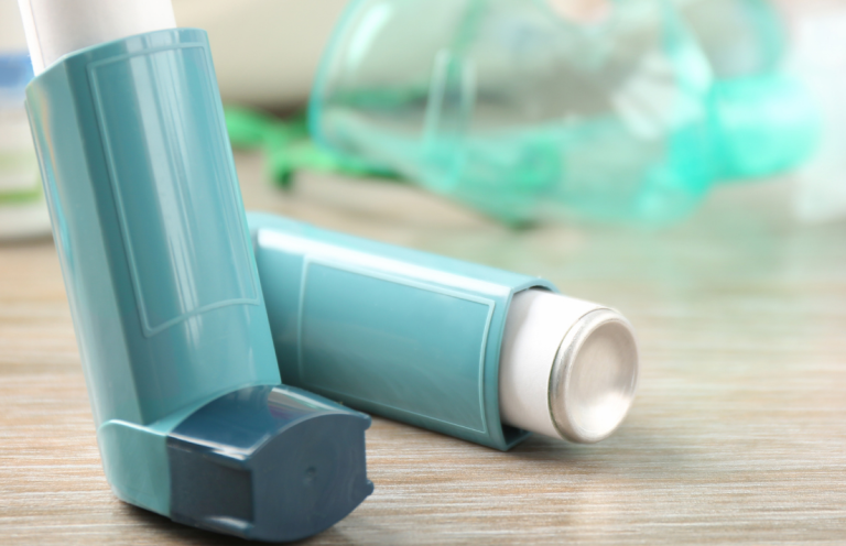 Two turquoise asthma inhalers resting on a wooden surface.