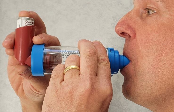 A woman using an asthma inhaler with a focused expression outdoors.