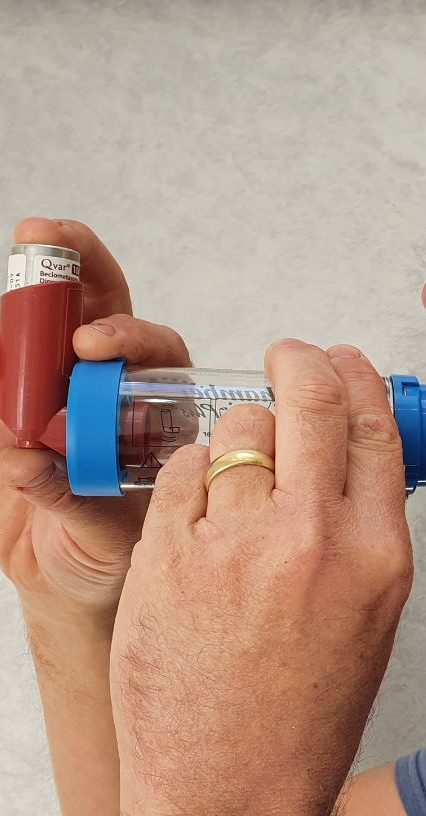 Syringe filled with red liquid, with vials in the background.