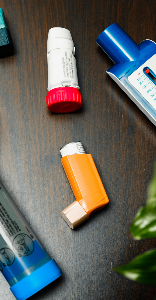 Assorted asthma inhalers and medication on a dark wooden surface.