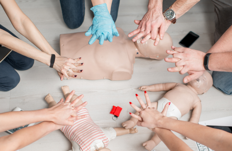 Hands performing CPR on training mannequins in a first aid class.