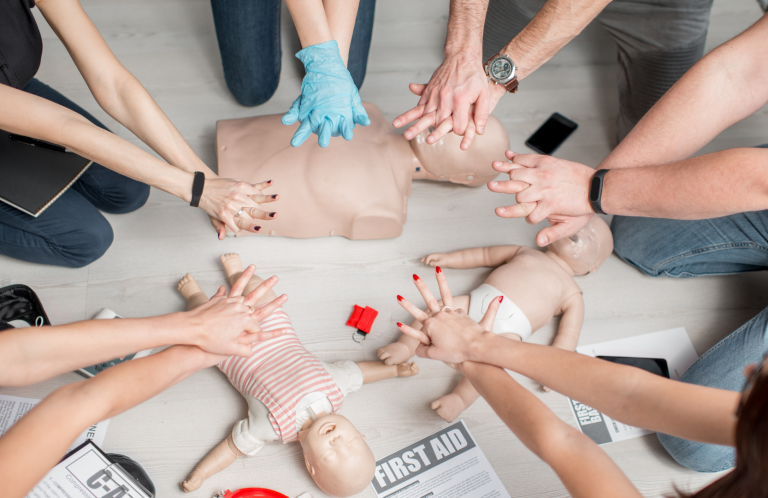 Hands performing CPR on infant mannequins during a first aid training session.