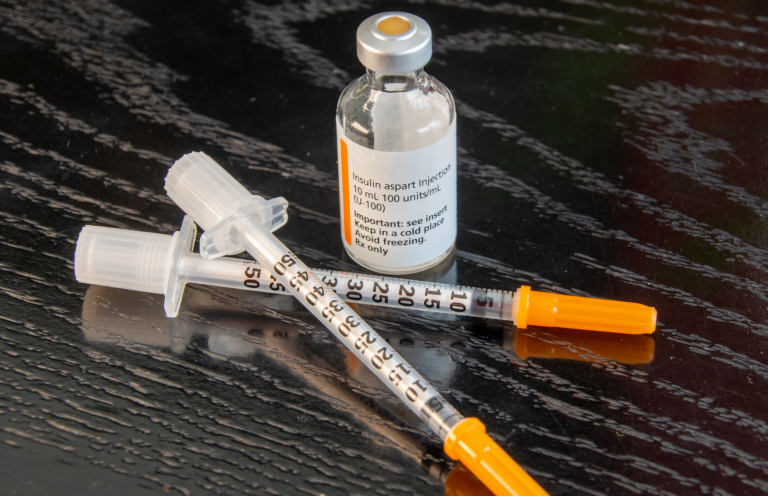 Insulin and two syringes with orange caps on a dark surface.