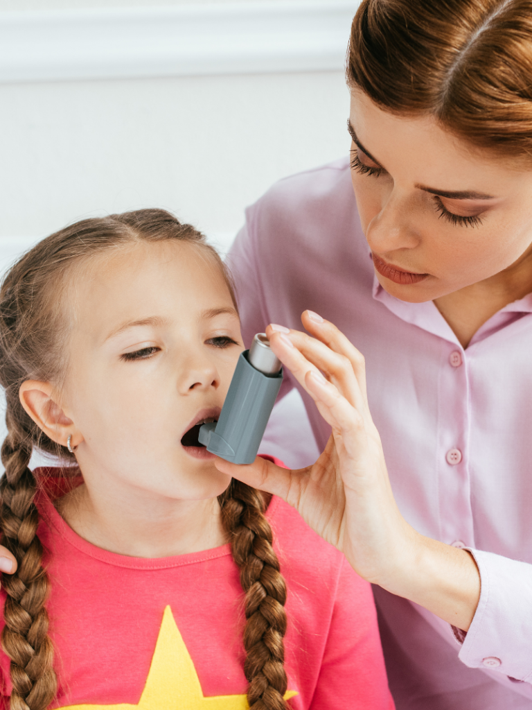 A woman assists a girl using an asthma inhaler.