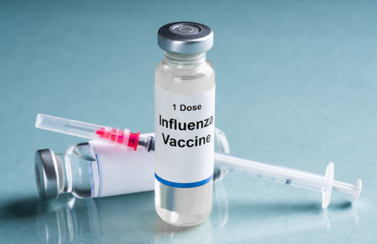 Immunisation and Vaccination Update Flu vaccine vial and syringe on a blue surface.