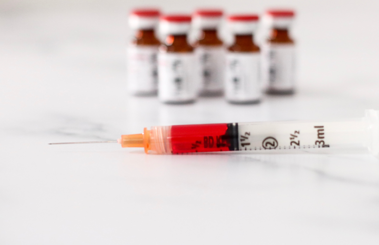 Syringe filled with B12 next to several brown vials on a marble surface.