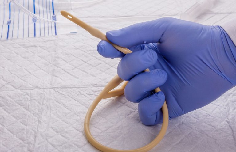 A gloved hand holding a flexible rubber catheter on a medical surface.
