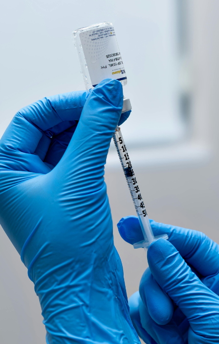 A gloved hand holds a syringe ready for vaccination with a vial in the background.