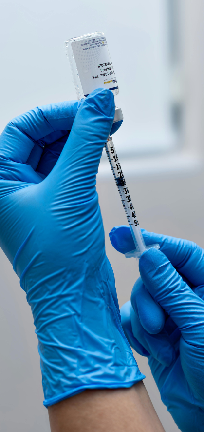 A gloved hand holds a syringe ready for vaccination with a vial in the background.