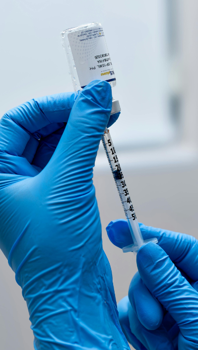 A gloved hand holds a syringe ready for vaccination with a vial in the background.